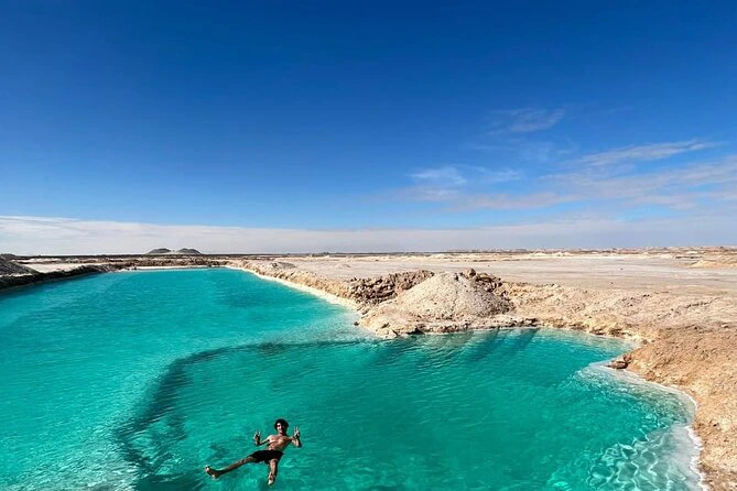 Traveler gazing at Siwa Oasis at sunset, surrounded by palm trees, salt lakes, and golden dunes.